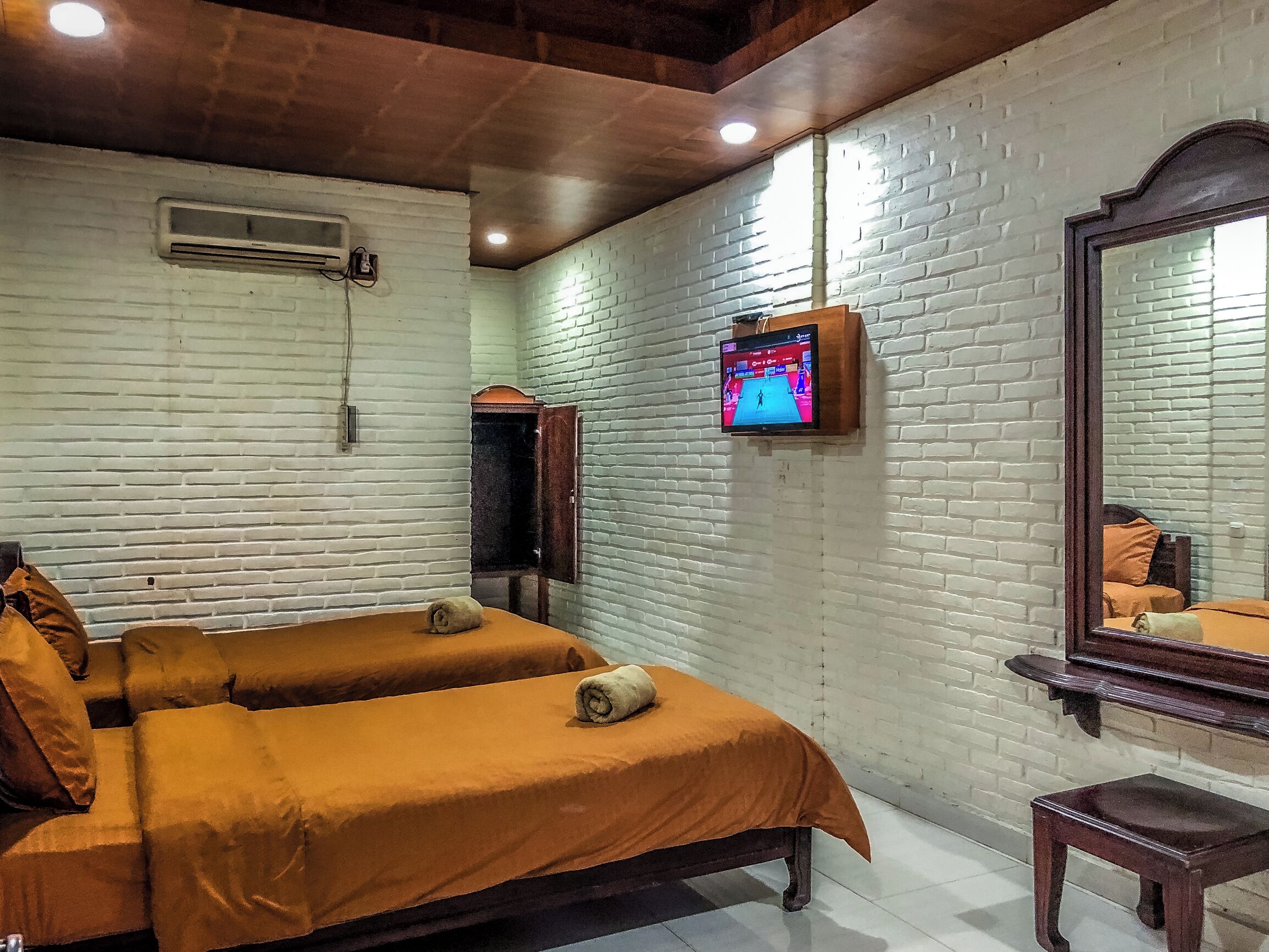 A hotel room with two beds, a TV mounted on the wall, a mirror, and a small wooden stool.