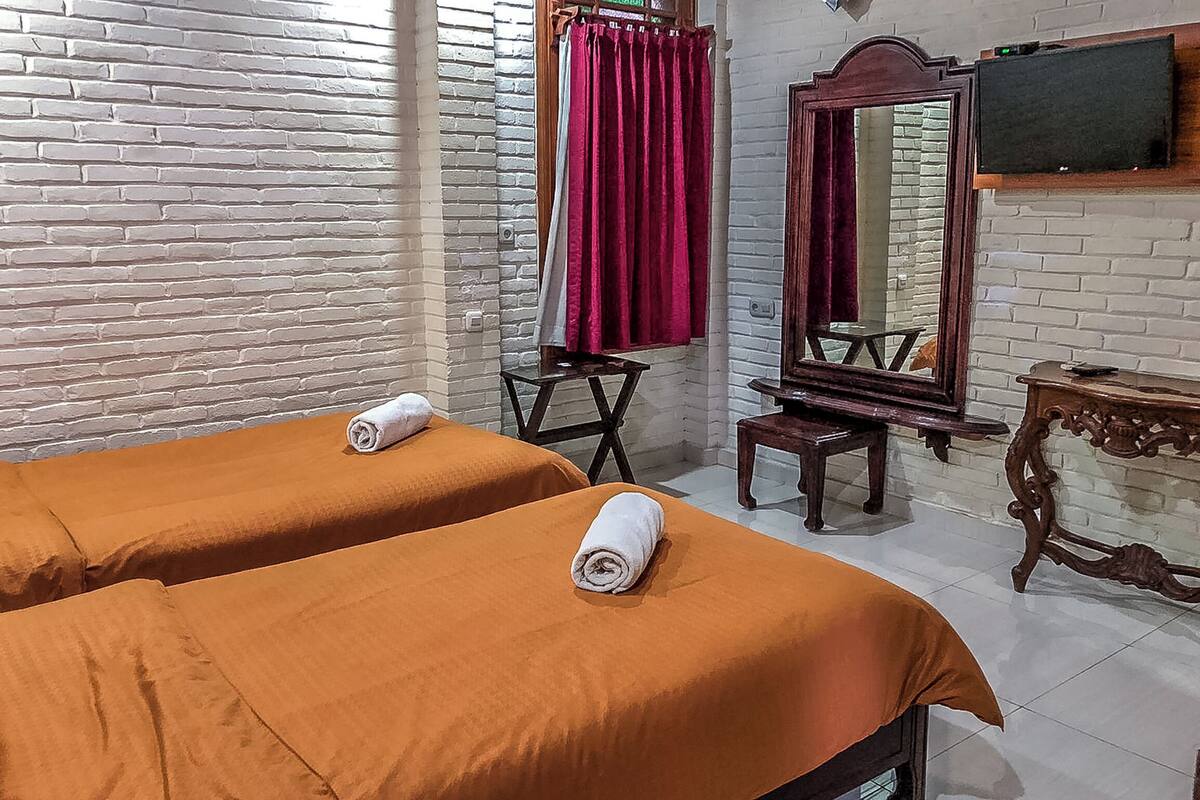 Une chambre d’hôtel avec deux lits, une chaise en bois, une petite table, un miroir et un téléviseur fixé au mur.
