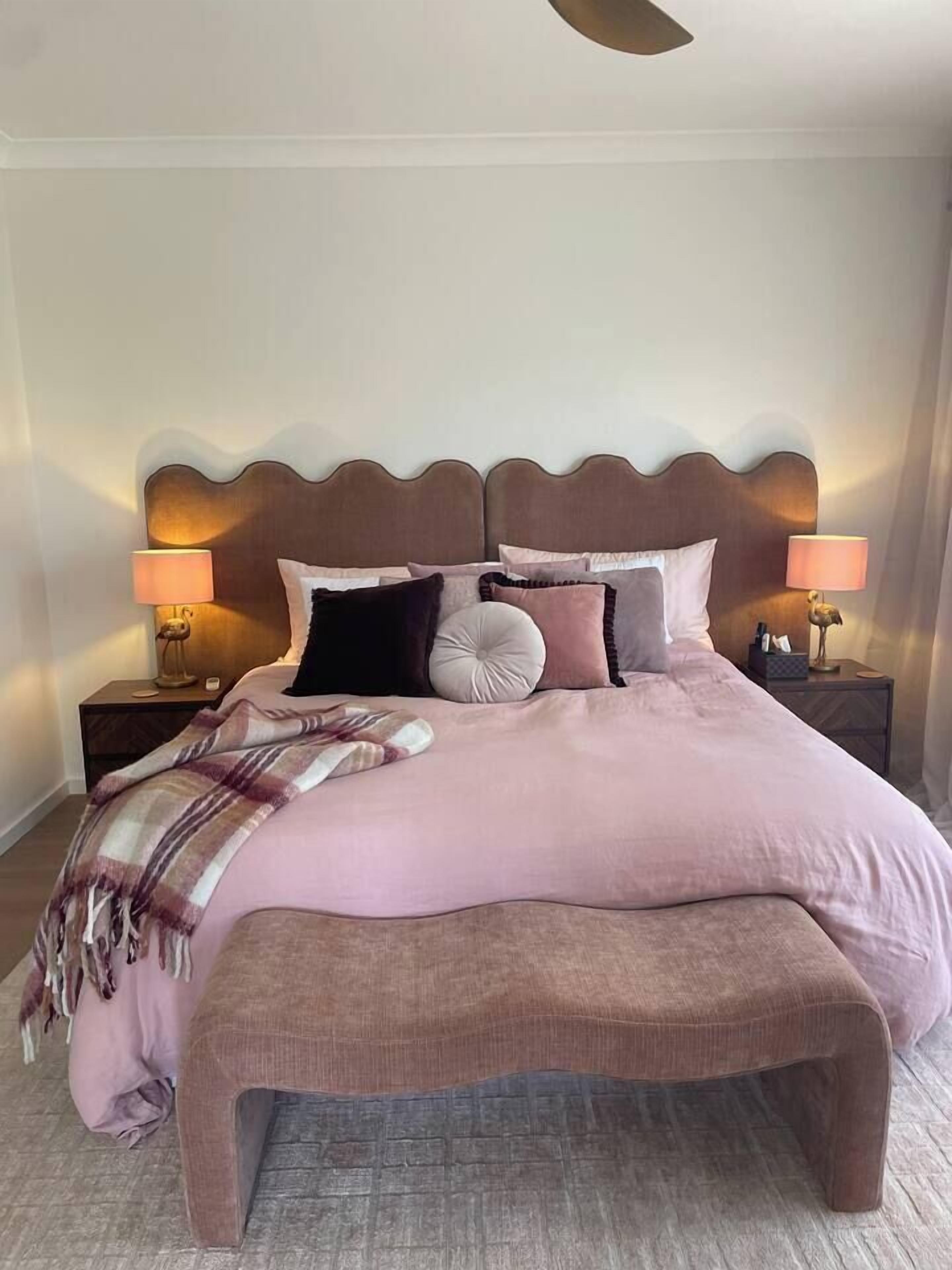 Een slaapkamer met een groot bed, twee nachtkastjes en een bankje.