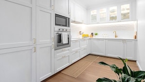 Una cocina moderna con muebles blancos, horno empotrado, microondas y un lavamanos con grifo dorado.