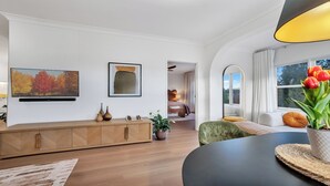 Una sala moderna con un mueble de madera, un televisor de pantalla plana, un cuadro y un comedor con una mesa y sillas.