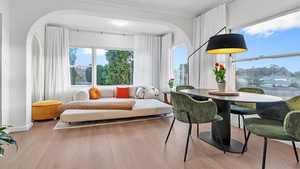 Una sala moderna con sofá, una mesa de comedor con sillas, una lámpara y vistas al exterior.