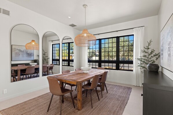 A dining area with a wooden table, chairs, and a large window with a view of greenery.