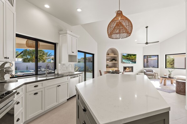 Una cocina moderna con armarios blancos, una isla grande y vista a una piscina.