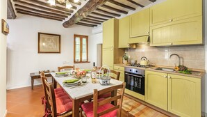 Une cuisine avec des poutres en bois, des meubles de couleur jaune et une table à manger agrémentée de coussins rouges.