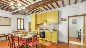 Une cuisine avec des meubles de couleur jaune, une table à manger avec des chaises et un plafond au style rustique.