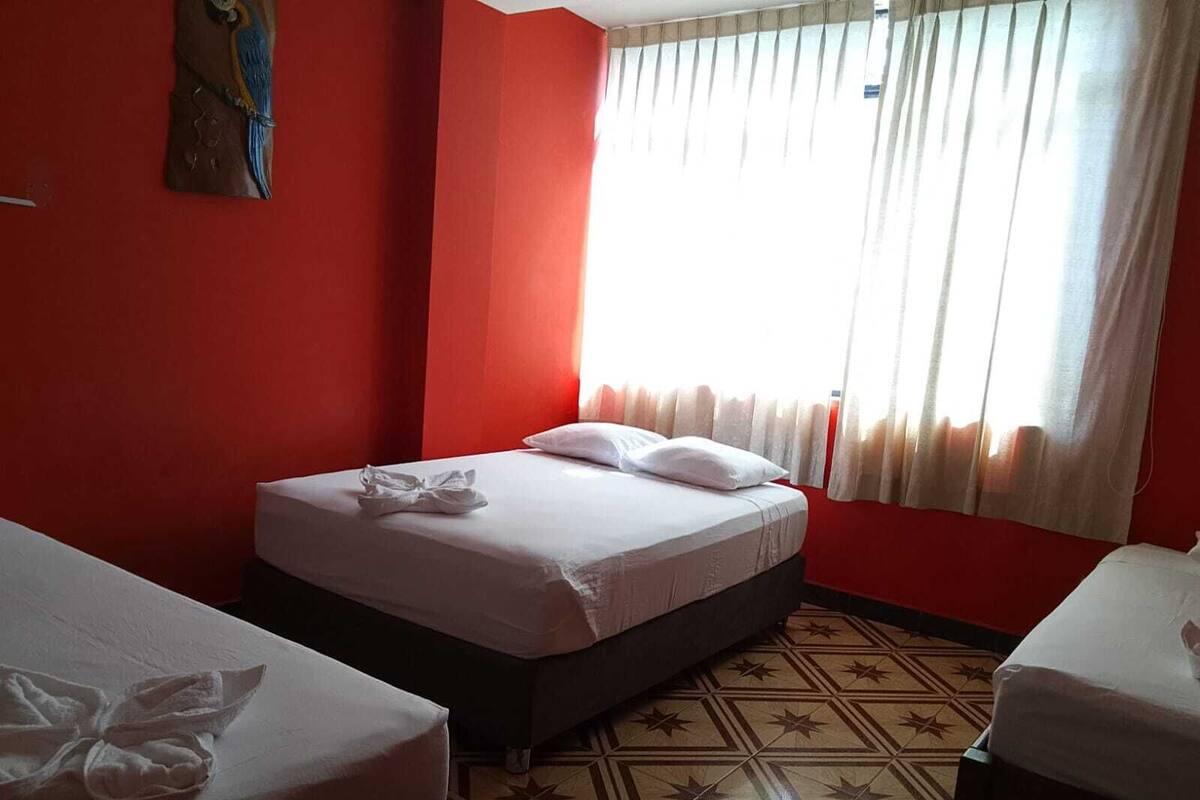 Une chambre d’hôtel avec un mur rouge, un sol à motifs et un lit avec une literie blanche et une serviette.
