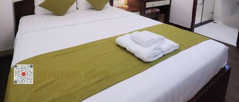 A hotel room with a bed, a bedside table with a lamp, a mirror, a small cabinet, and a bathroom with a sink and mirror.