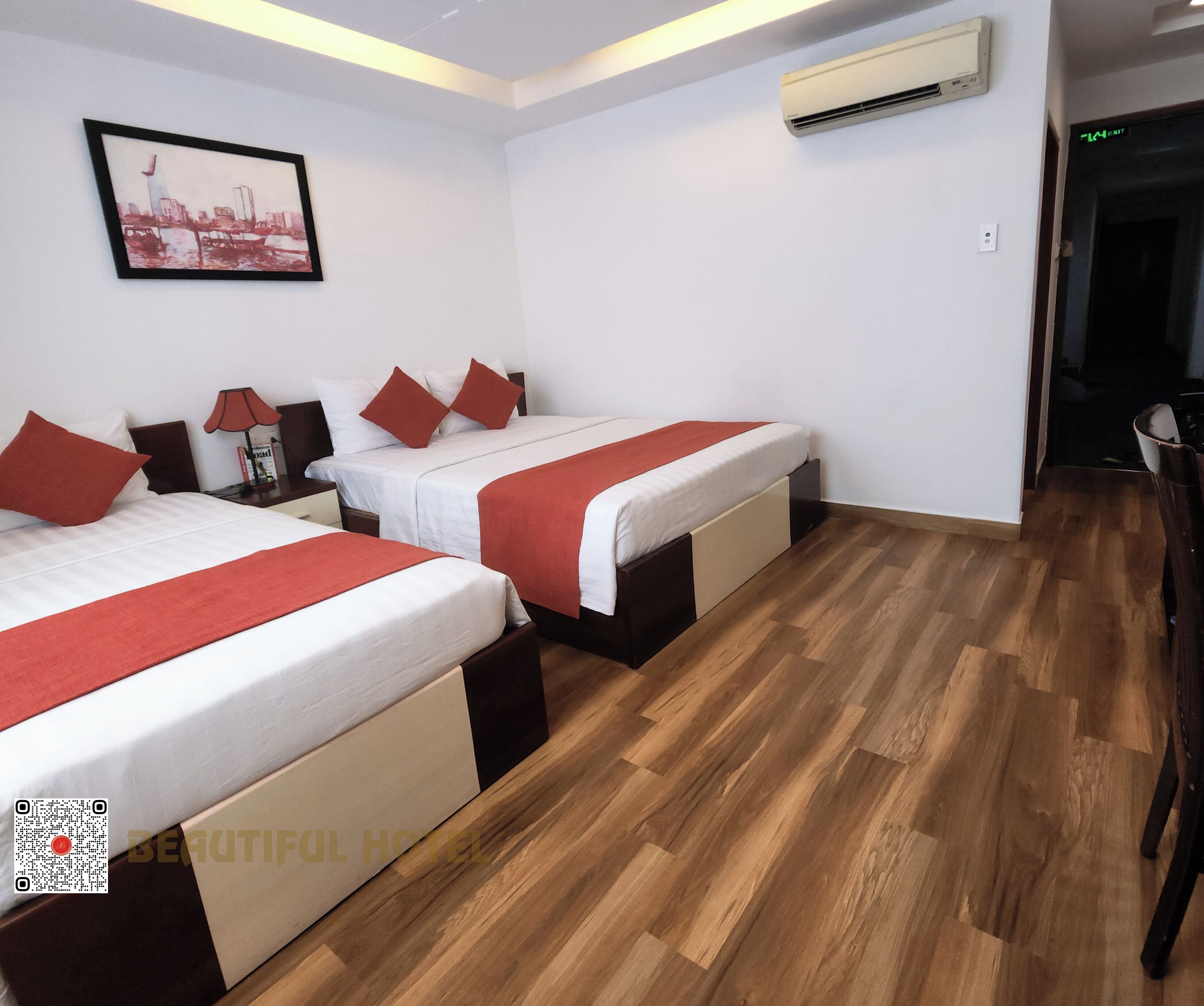 Habitación de hotel con dos camas, un cuadro de un paisaje urbano, un equipo de aire acondicionado y piso de madera.