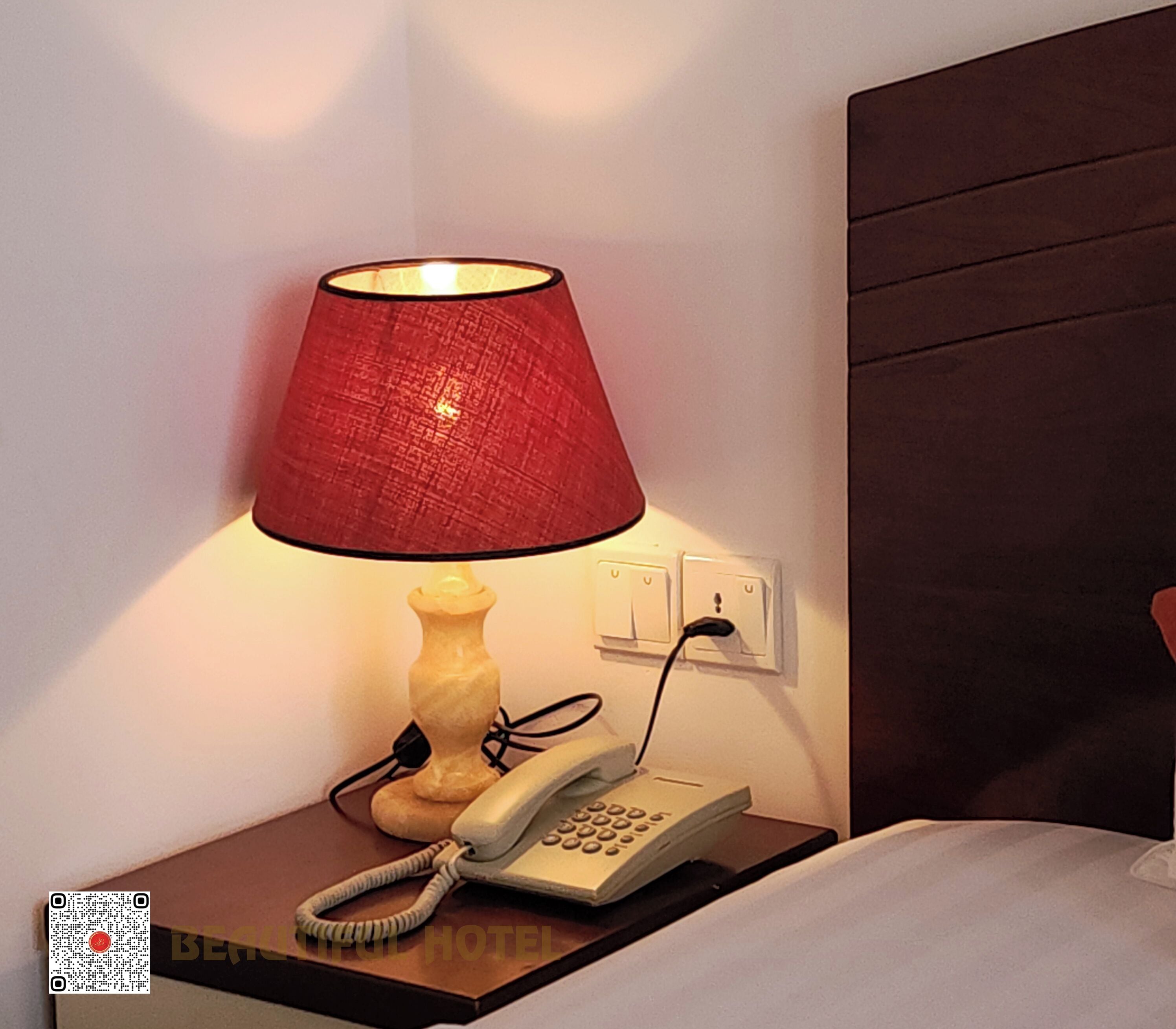 Ein Nachttisch mit Lampe, Telefon und Steckdose.