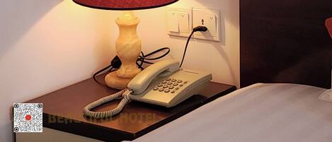 Ein Nachttisch mit Lampe, Telefon und Steckdose.