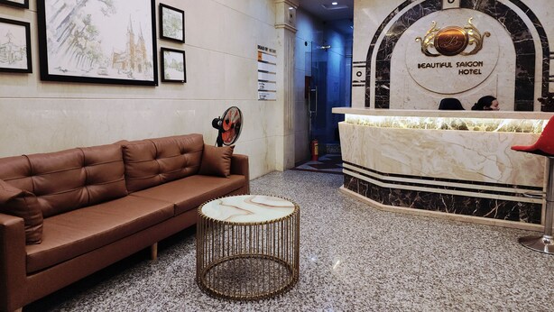 A lobby with a brown leather sofa, a round coffee table, and a reception desk with a marble top. - Beautiful Hotel Bui Vien (Ho Chi Minh City)