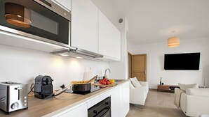Una cocina moderna con tostadora, cafetera y estufa. Hay una zona de comedor con sofá y televisor de pantalla plana.