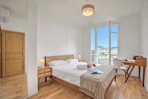 A hotel room with a bed, bedside tables, a desk, and a view of the city.