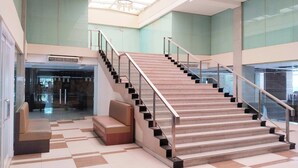 A spacious lobby with a central staircase, a seating area, and a glass entrance. - Shankee Sudirman (Jakarta)