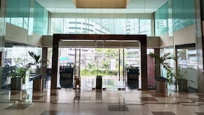 A modern hotel lobby with a glass entrance, potted plants, and a view of the cityscape. - Shankee Sudirman (Jakarta)