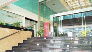 A staircase leading to an ATM Centre with a glass entrance, a wet floor sign, and a sign for room availability for rent. - Shankee Sudirman (Jakarta)