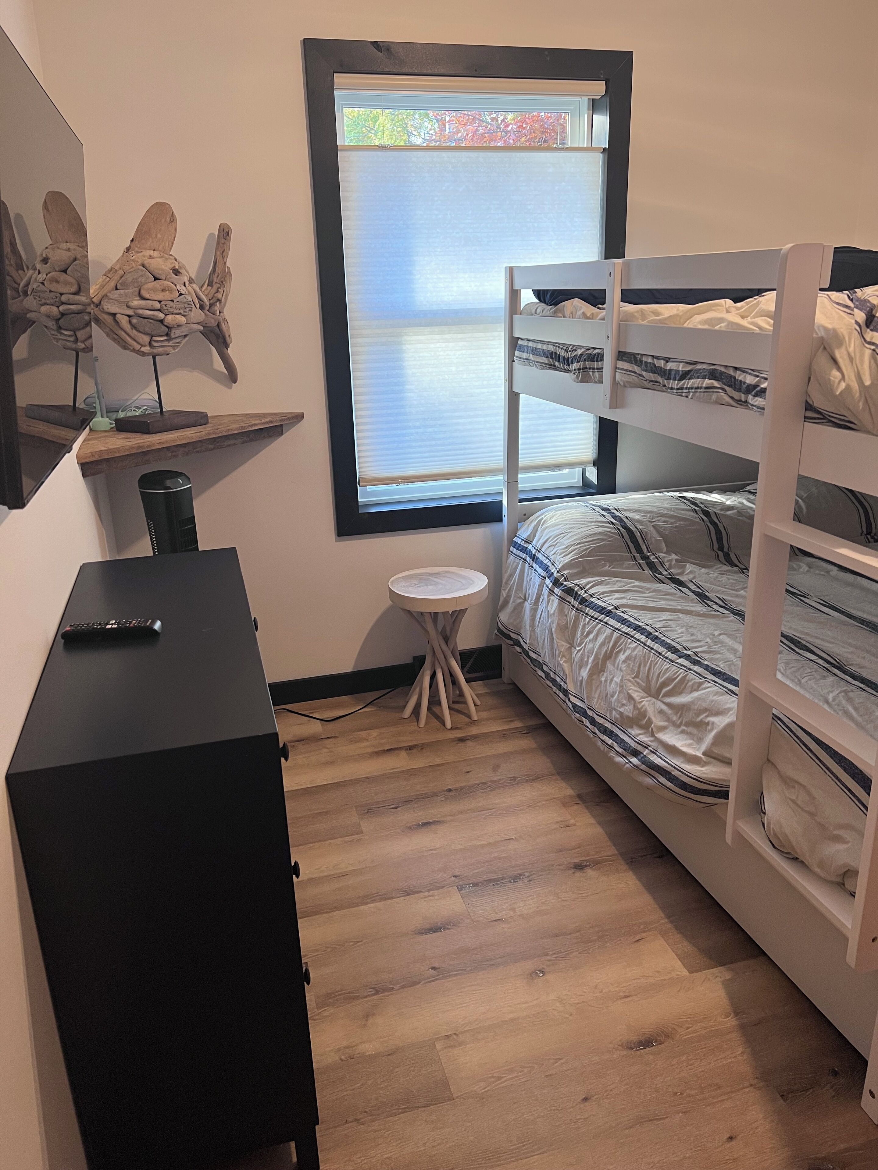 Une chambre avec un lit superposé, un bureau avec un ordinateur, une petite table ronde et une fenêtre avec des stores.