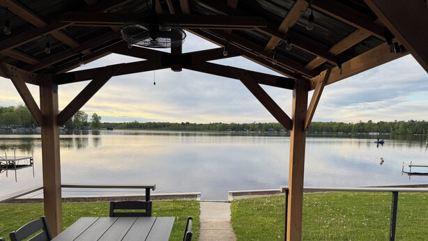 A covered outdoor seating area with a view of a calm lake and dock. - Over 200’ of  lakefront all sand on Washington lake with a view of Shawano lake! (Shawano)