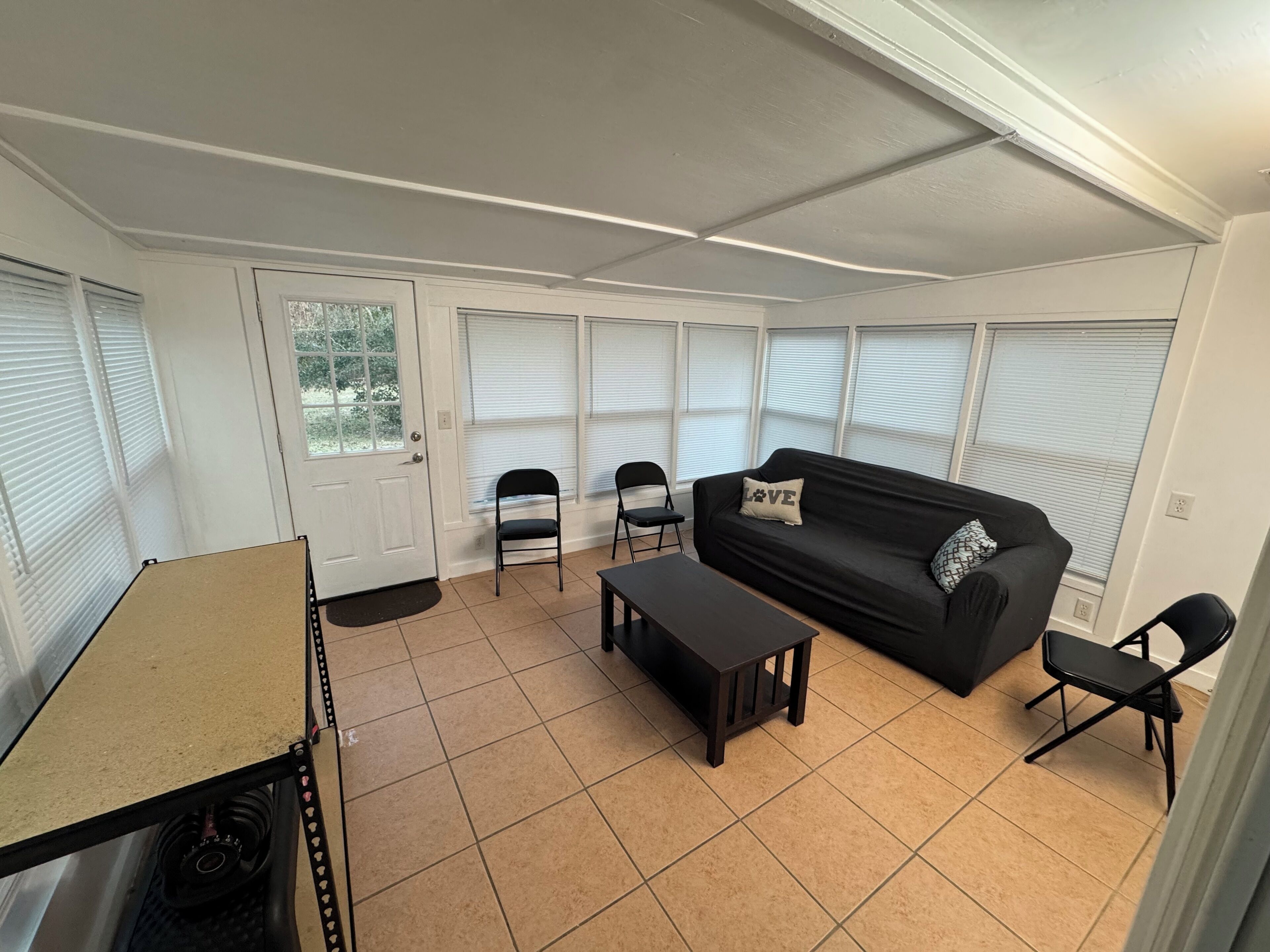 A living room with a black sofa, two chairs, a coffee table, and a door with a window.