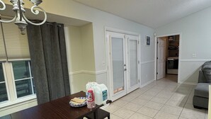 A dining area with a wooden table and bench, a chandelier, and a window with curtains.