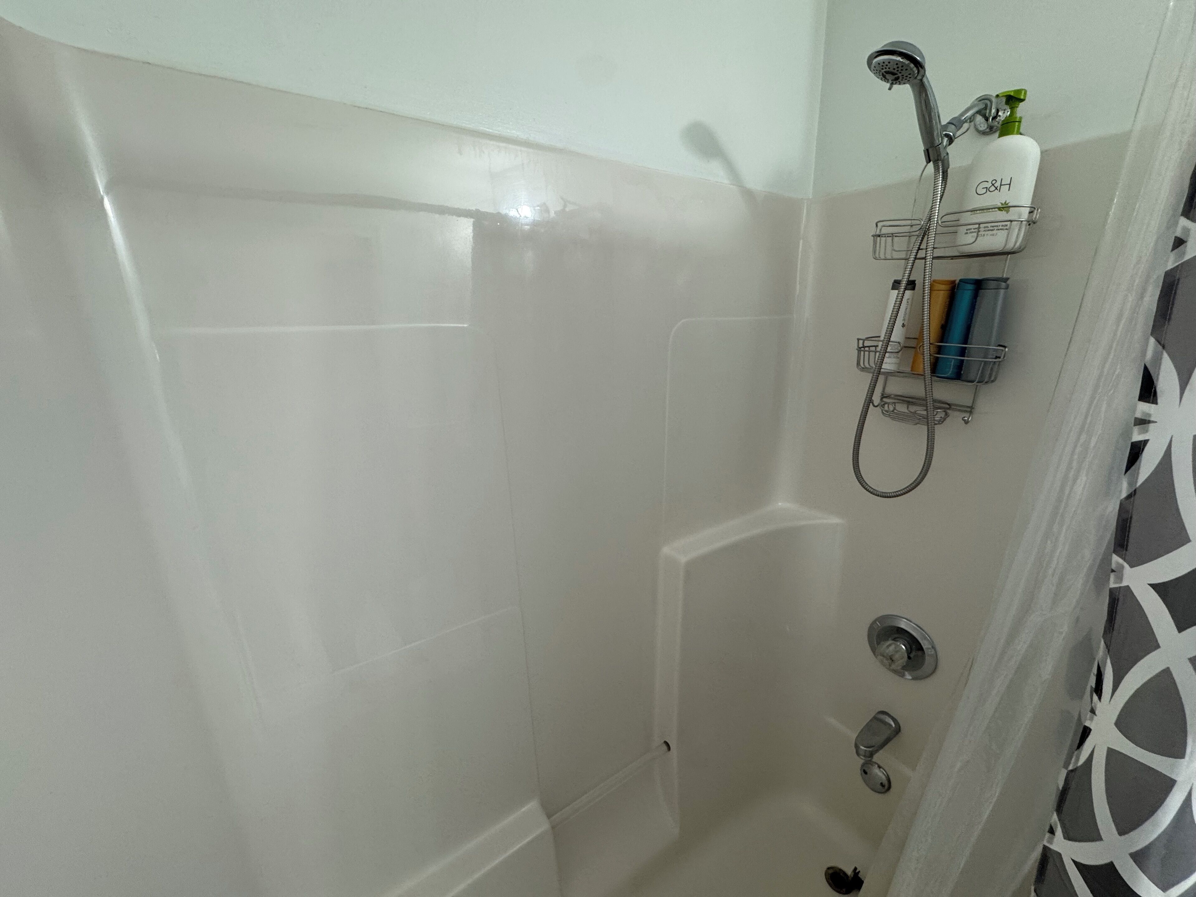 A shower with a handheld showerhead, a wall-mounted soap dispenser, and a soap dish with multiple bottles.