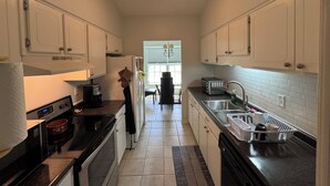 A narrow kitchen with white cabinets, a black countertop, a microwave, a stove, and a sink.