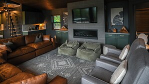 Ein modernes Wohnzimmer mit einer großen Eckcouch, einem grauen Sessel und einem runden Couchtisch. Ein Flachbildfernseher ist an der Wand über einem Kamin befestigt.