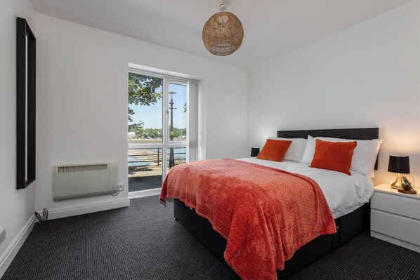 A modern bedroom with a large bed, a nightstand, a heater, and a view of the outdoors.