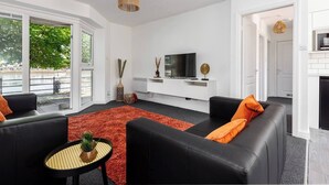 Ett modernt vardagsrum med svarta soffor i läder, en röd matta och en tv placerad på en vit tv-bänk.