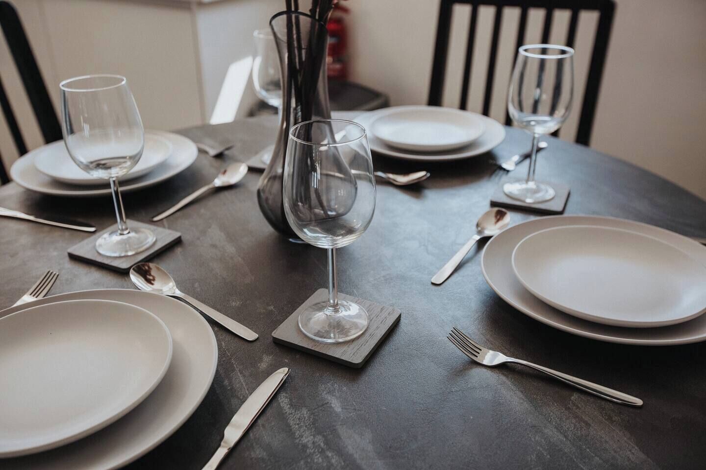 Una mesa de comedor dispuesta con platos, cubiertos y copas de vino, centrada con un florero.