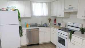 Una cocina moderna con armarios blancos, un refrigerador de acero inoxidable, lavavajillas, microondas, estufa y una ventana con cortinas de gasa.