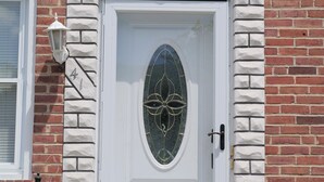 A white door with a decorative glass panel, a small bird emblem above it, and a brick wall with a white stone border.