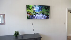 Un televisor montado en una pared blanca, con un aparador de madera oscura debajo.