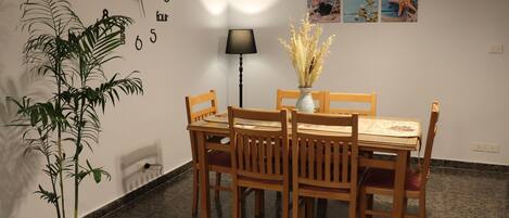 Un comedor con mesa y sillas de madera, una planta en maceta, un reloj de pared y una lámpara.