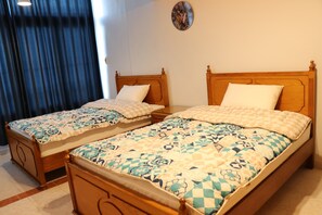 Two wooden beds with checkered bedding, a wall clock, and a window with curtains.