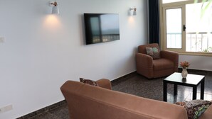A living room with a flat-screen TV mounted on the wall, two wall-mounted lamps, a brown leather sofa, a matching armchair, and a small table with a vase of flowers. -  NOUR1
Sea view (Alexandria)