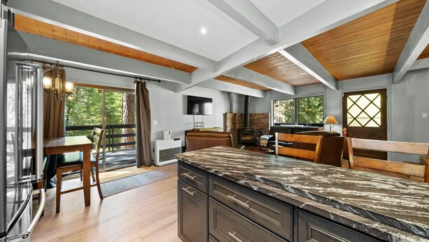 A modern kitchen with a large island, wooden beams, and a fireplace. - Escape to Tranquility in This Beautiful Forest-Edge Retreat (Graeagle)