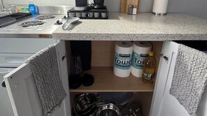 Cocina compacta con microondas, hervidor y tostadora. Hay dos rollos de papel de cocina y una botella de detergente para platos en la encimera.