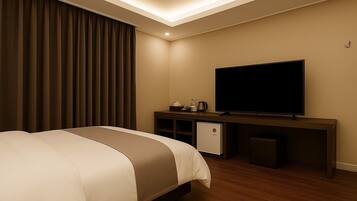 Habitación de hotel con cama, televisor, mini refrigerador y escritorio con cafetera.