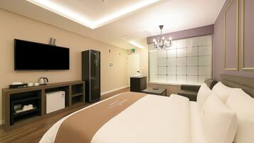 A modern hotel room with a large bed, a flat-screen TV, a minibar, a seating area, and a large window with a view.