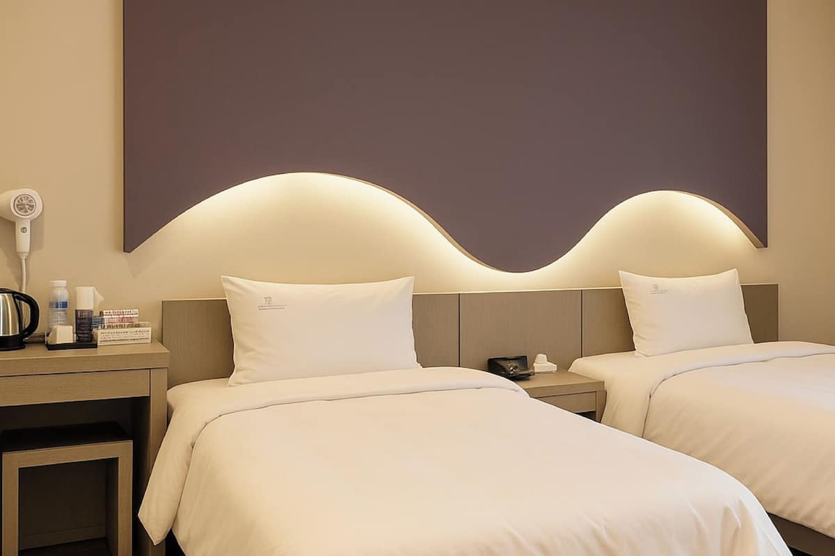 A hotel room with two beds, a nightstand with a hairdryer, and a wall-mounted light fixture.