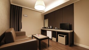 Kompakti hotellihuone, jossa on sohva, pieni pöytä, televisio, minijääkaappi ja mikroaaltouuni.