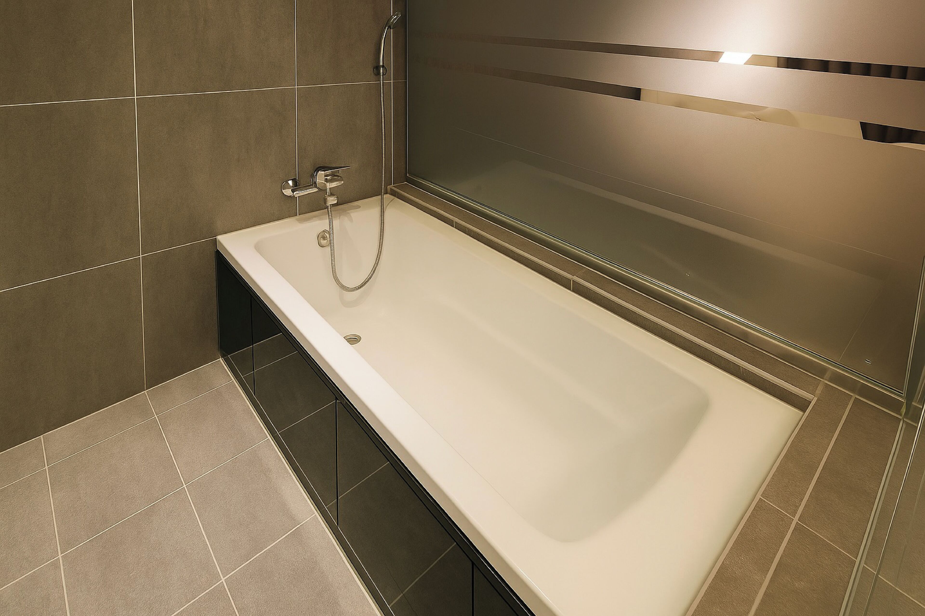 A modern bathroom with a bathtub, a shower, and a glass partition.