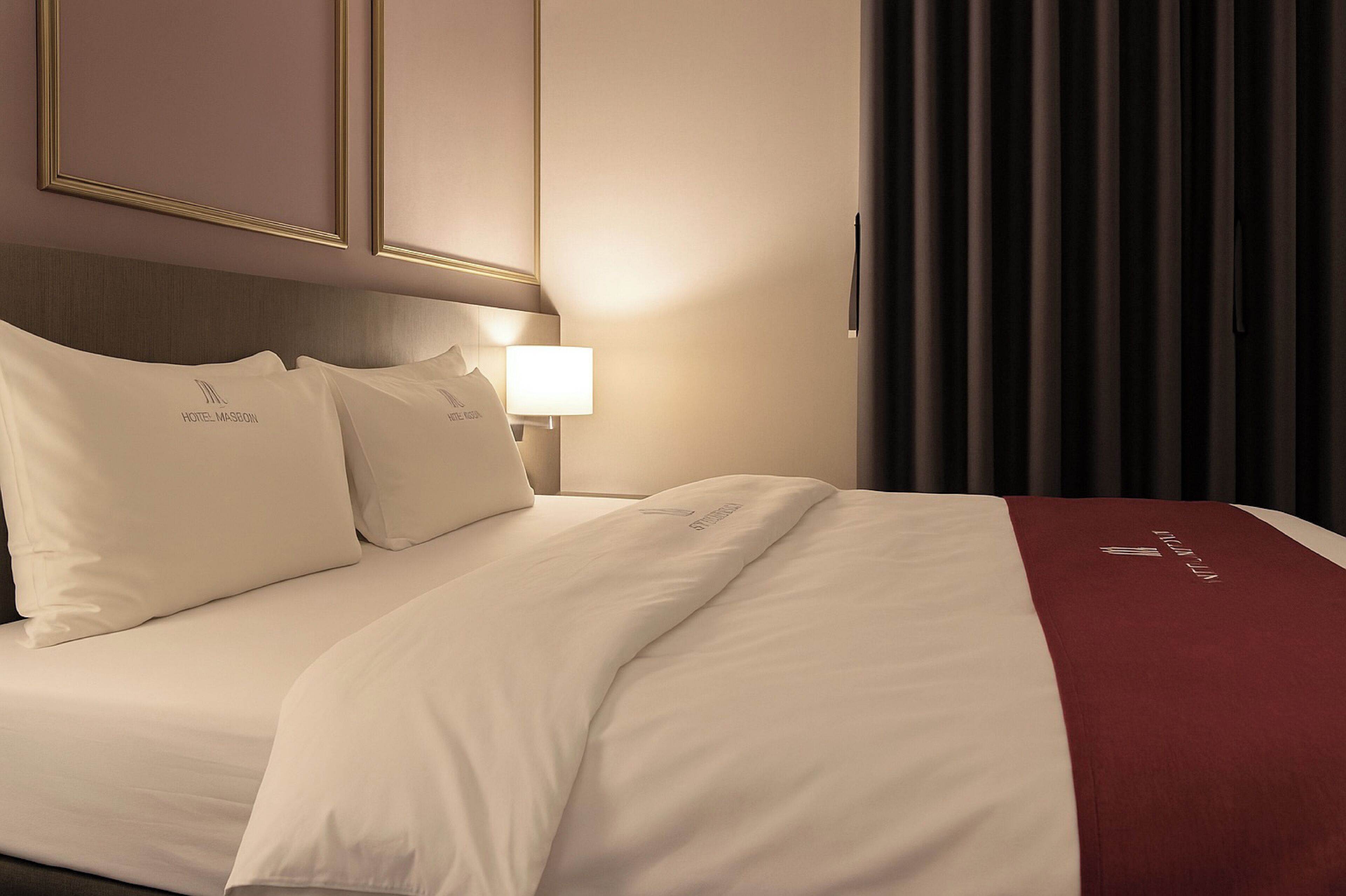 Habitación de hotel con una cama bien hecha, una lámpara de noche y vistas al exterior por la ventana.
