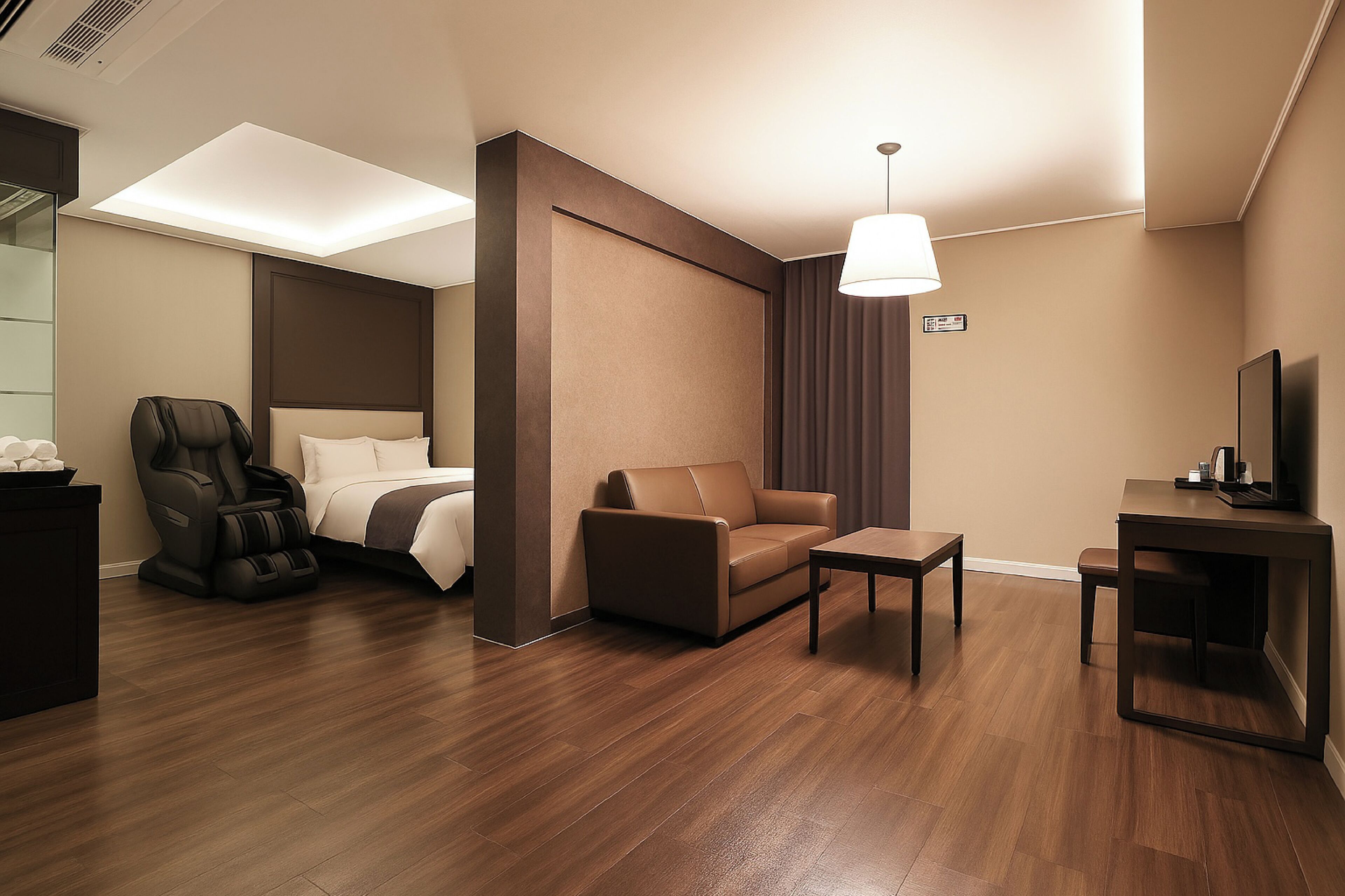A modern hotel room with a bed, massage chair, sofa, and a small table.