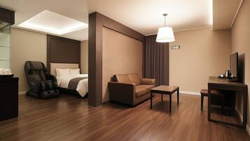 A modern hotel room with a bed, massage chair, sofa, and a small table.