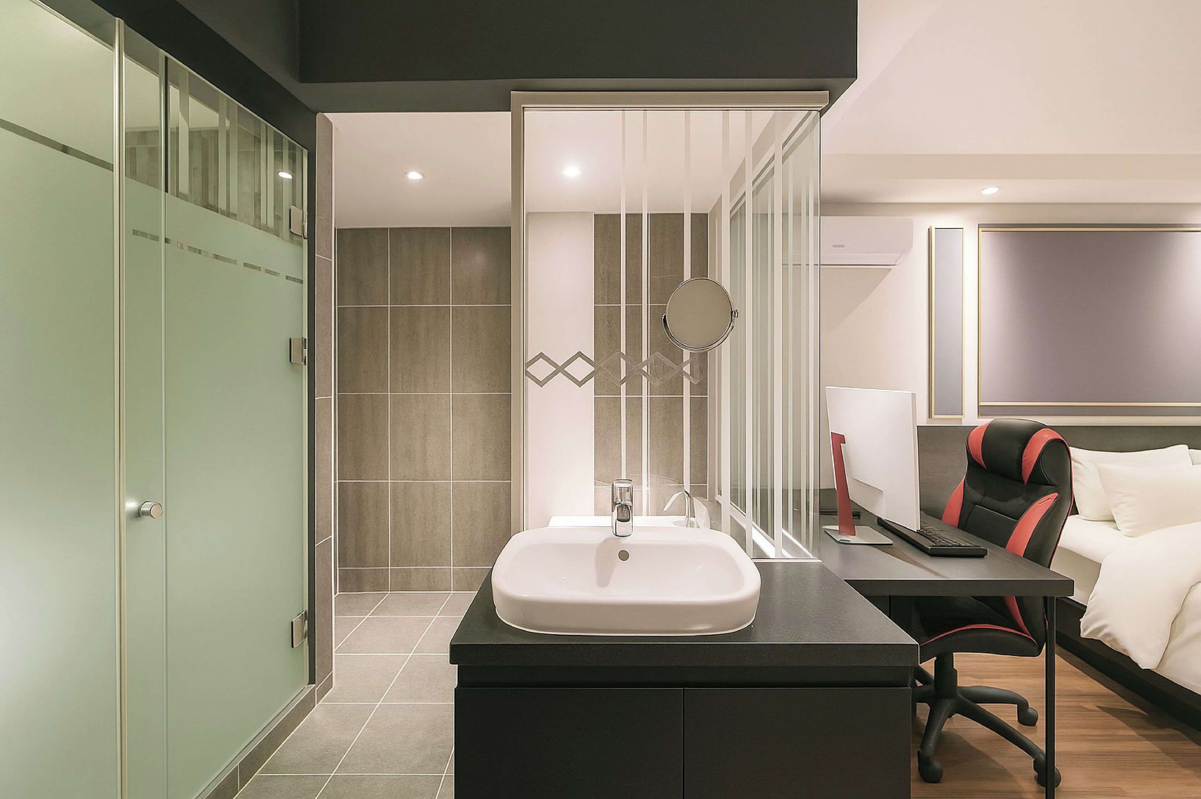 A modern hotel bathroom with a sink, mirror, and shower area.