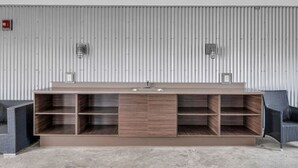En modern, minimalistisk receptionsdisk med inbyggda hyllor, två väggmonterade lampor och en enkel vägg av korrugerad metall i bakgrunden.