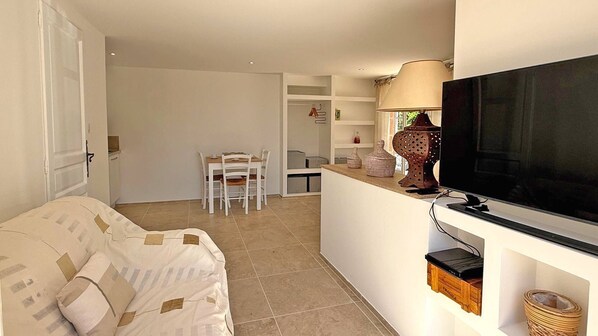 A compact living space with a sofa, a dining area with chairs, a TV mounted on a wall, and a lamp.
